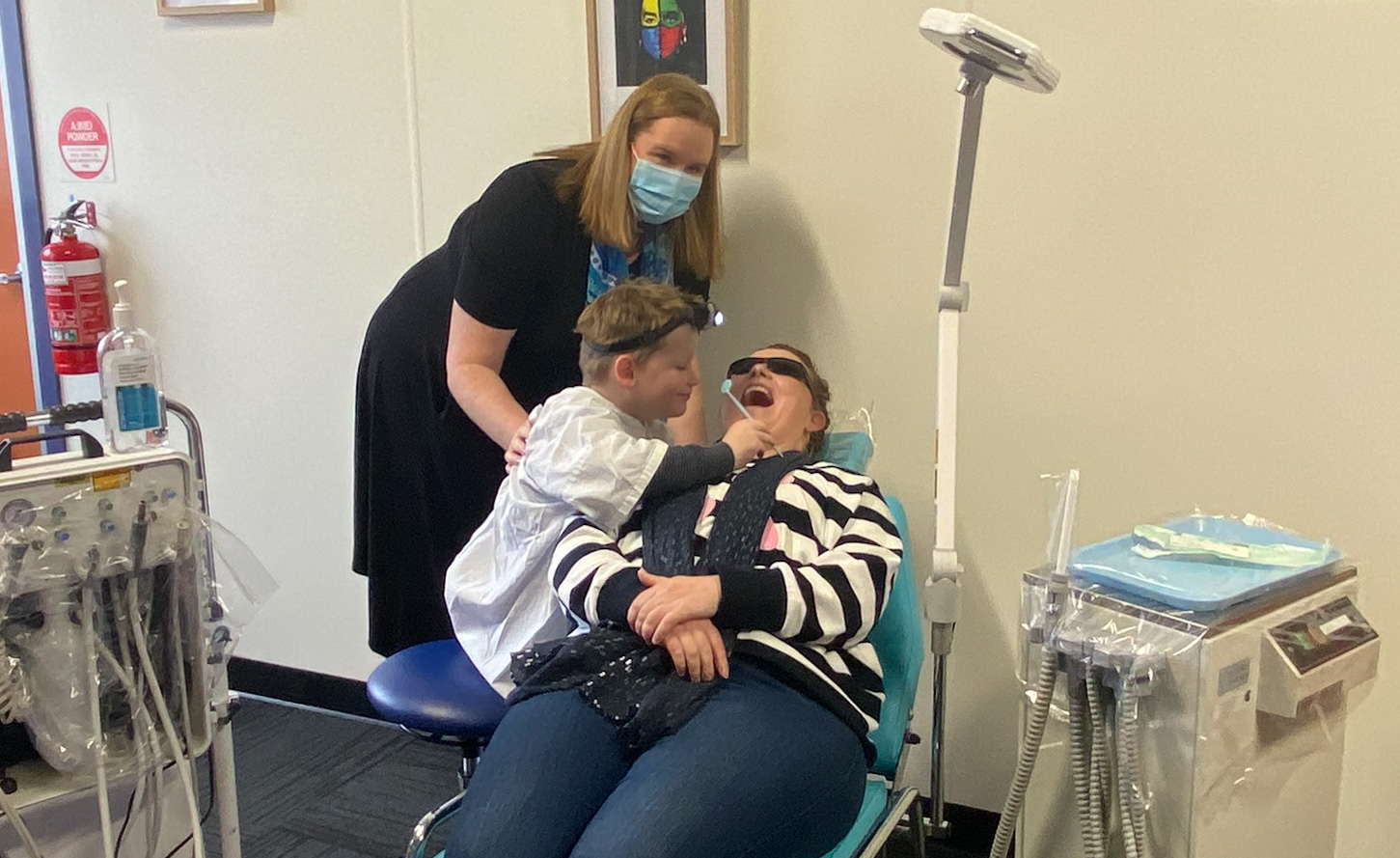 Jodie Robinson (Clinical Coordinator, Dental Services Grampians Health) watches on as Cooper treats his mum and Grampians Health Oral Health Educator, Courtney Liversage in a mobile dental clinic